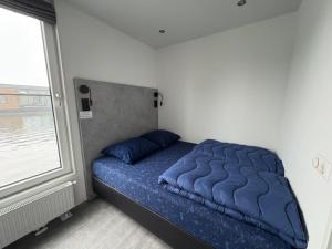 a bed with a blue comforter in a room with a window at De Maasterp - Watervillage 14 in Ohé en Laak