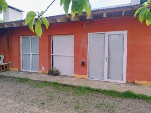 ein rotes Gebäude mit drei Türen und einem Stuhl in der Unterkunft Lo de Juana in Puerto Madryn