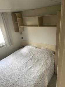 a bedroom with a bed with white sheets and shelves at Cosy Mobil-Home climatisé in Aureilhan