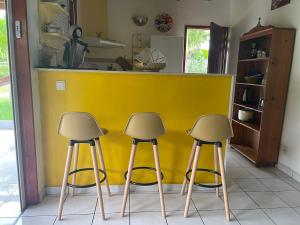a kitchen with three stools in front of a yellow counter at Bungalow Ludivine in Sainte-Anne