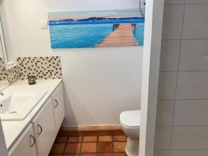 a bathroom with a toilet and a painting of a pier at Cosy Studio in La Trinité