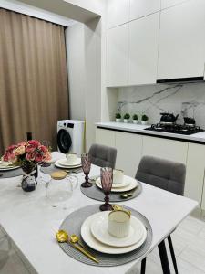 a white kitchen with a table with plates and glasses at Lumiere in Aktau +5 photos