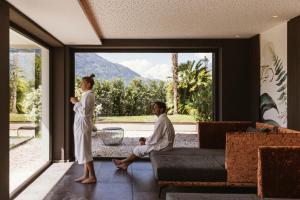 a man and woman standing in a living room looking out the window at Hotel Paradies in Tirolo
