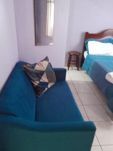 a living room with a blue couch and a bed at Suíte em casa compartilhada a poucos metros da praia in São Sebastião