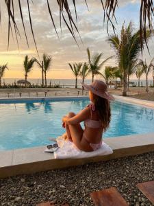 a girl in a bikini and hat sitting next to a swimming pool at Wallac Bungalows Canoas de Punta Sal in Canoas De Punta Sal