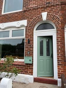 eine grüne Tür an der Seite eines Backsteingebäudes in der Unterkunft Victorian Inspired Home in Stockport