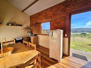 a kitchen with a table and a refrigerator in a room at Chalés Pão Sobre as Águas - a 5 minutos de cachoeiras e vista maravilhosa do pôr do sol in Carrancas