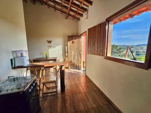 a kitchen with a table and a large window at Chalés Pão Sobre as Águas - a 5 minutos de cachoeiras e vista maravilhosa do pôr do sol in Carrancas