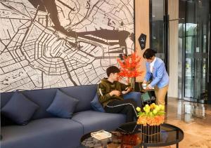 two people standing in a living room with a blue couch at Echarm Hotel Nanjing Lishui High-speed Railway Station Wuzhou Commercial City in Lishui