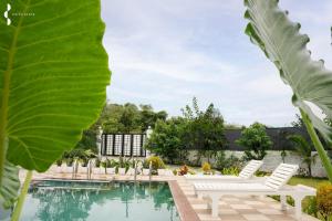 een zwembad met witte stoelen en een groot blad bij Privy Stays- Cavo Villa, Alibag in Mān