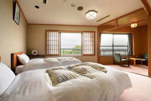 a bedroom with two beds and a table and windows at Shintomi-tei in Matsushima
