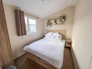 a bedroom with a bed with white sheets and a window at Great Caravan With Central Lounge & Wifi At Broadland Sands, Suffolk Ref 20070Bs in Hopton on Sea