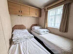 two beds in a small room with a window at Lovely 6 Berth Caravan With Decking At California Cliffs In Scratby Ref 50048L in Great Yarmouth