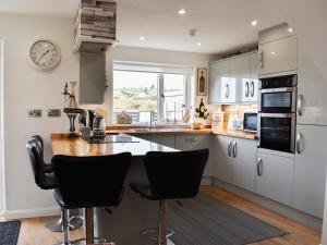 a kitchen with white cabinets and a counter with black chairs at Mountain View in Morfa Bychan +17 photos