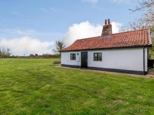 a white building with a red roof in a field at Pettingalls Farm Cottage in Great Ellingham