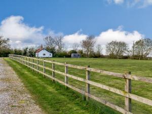 a wooden fence in a field with a white house at Pettingalls Farm Cottage in Great Ellingham
