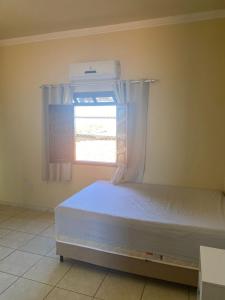 Un dormitorio con una cama blanca con una ventana. en Casa Doce Refugio - ao lado do centro, en Bom Jesus da Lapa