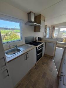 Una cocina con fregadero, estufa y ventana. en 2 Bedroom Caravan, New Beach Holiday Park, en Dymchurch