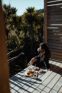 a woman sitting on a table with plates of food at Hahei Tiny Home - Outdoor Bath in Hahei