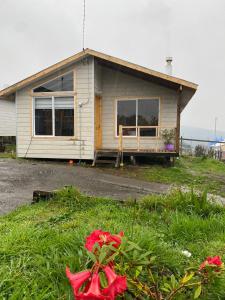 Una pequeña casa con ventanas y flores delante de ella. en Cabañita Ten Ten Vilú, en Quellón