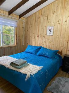 1 dormitorio con 1 cama azul y paredes de madera en Cabañita Ten Ten Vilú, en Quellón