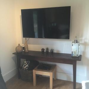 a television hanging on a wall with a table with a shelf at Willow Court Farm The Lodge & Petting Farm, 8 mins from Legoland & Windsor, 15 mins from Lapland UK in Windsor
