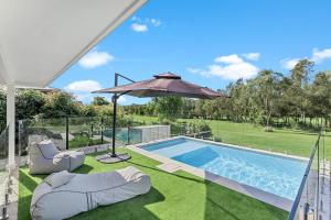 ein Swimmingpool mit Sonnenschirm und Stühlen neben einem Pool in der Unterkunft Whitepepper Cottage in Pokolbin