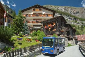 un autobús azul conduciendo por una carretera frente a un edificio en Hotel Romantica en Zermatt
