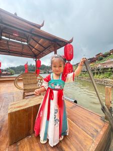 a little girl in a chinese dress on a boat at ริมหมอก จาต๋ารักไทย in Ban Rak Thai +9 photos
