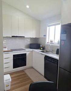 a kitchen with white cabinets and a black dishwasher at The Cottage in Moruya +7 photos
