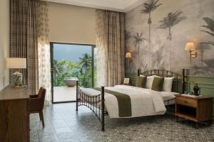 a bedroom with a bed and a desk and a window at The Ranch Kakkadampoyil - a VKation Experience in Kakkadampoyil