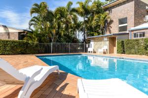 a swimming pool with two white chairs next to a house at Smart Motels Bert Hinkler in Bundaberg