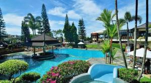 a pool at a resort with palm trees and bushes at Purnama Hotel in Malang