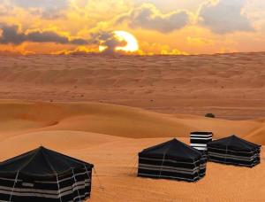 Badīyahlayali camp的沙漠中的三个帐篷,背景是日落