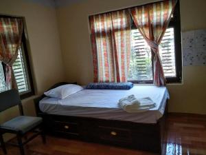 a bed in a bedroom with two windows and a chair at Home stay number 11 , Ramechhap, Manthali in Rāmechhāp