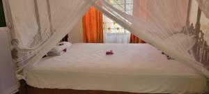 a white bed with white curtains and purple flowers on it at Paul's House in Nungwi +4 photos