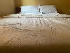 1 cama no hecha con sábanas y almohadas blancas en Chikawaga Lodge, en Blantyre