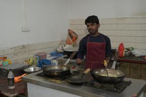 a man in a kitchen cooking food in wok at Nap Of Joy in Jāmb +7 photos