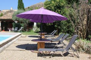 a table with a purple umbrella and chairs next to a pool at Maison d'hôtes Ferme de la Commanderie in Richerenches