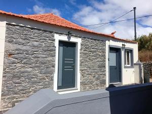 a stone cottage with blue doors and a stone wall at Adelaide's Cottage in Ponta do Pargo