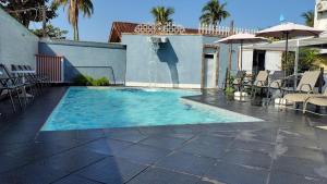 ein Swimmingpool mit Liegestühlen und Sonnenschirmen neben einem Haus in der Unterkunft Hotel Pousada Iracemar, 60m da Praia da Enseada, Piscina Aquecida ao Ar Livre para Relaxar em Qualquer Estação, Café da Manhã, Estacionamento, Recepção 24h, Aproveite o Mar, Passeios e Atividades Náuticas a 100 metros in Guarujá + 21 Fotos
