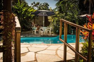 une piscine avec un parasol et des gens assis à une table dans l'établissement Pousada Fênix, à Pirenópolis
