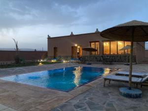 una piscina con una sombrilla delante de una casa en Tigmi Timhar, en Nkob