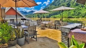 a patio with tables and umbrellas with mountains in the background at Dokchampa River View Villa in Nongkhiaw