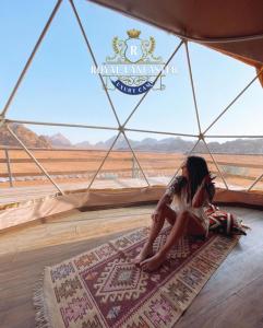 DisahにあるROYAL LANCASTER lUXURY CAMPのテントの中で敷物の上に座って砂漠を眺める少女