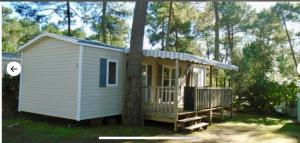 a small white shed with a porch next to a tree at Mobil home bonne anse plage in Les Mathes