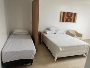 a bedroom with two beds and a chair at Quarto in São Francisco do Sul