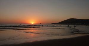 a sunset on a beach with people in the water at Appartement à usage familial in Agadir +4 photos