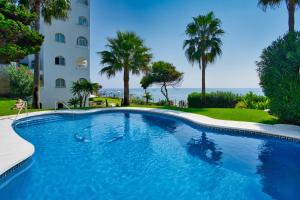 a swimming pool in front of a building with palm trees at Beachfront Haven in Mijas Costa