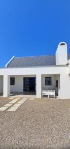un edificio blanco con un banco delante en De Meye Jacobsbaai, en Jacobs Bay